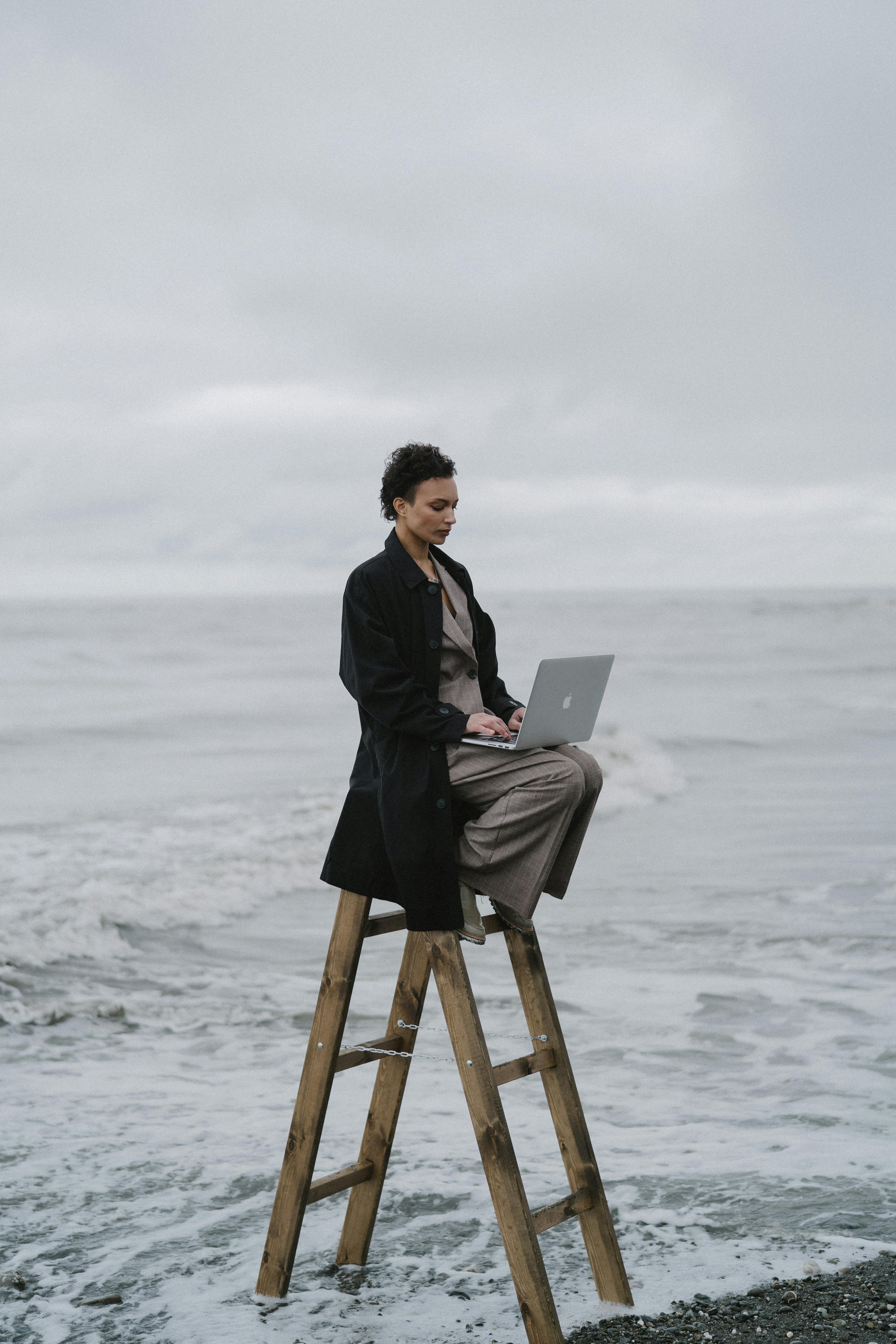 Woman sitting on ladder in ocean with computer