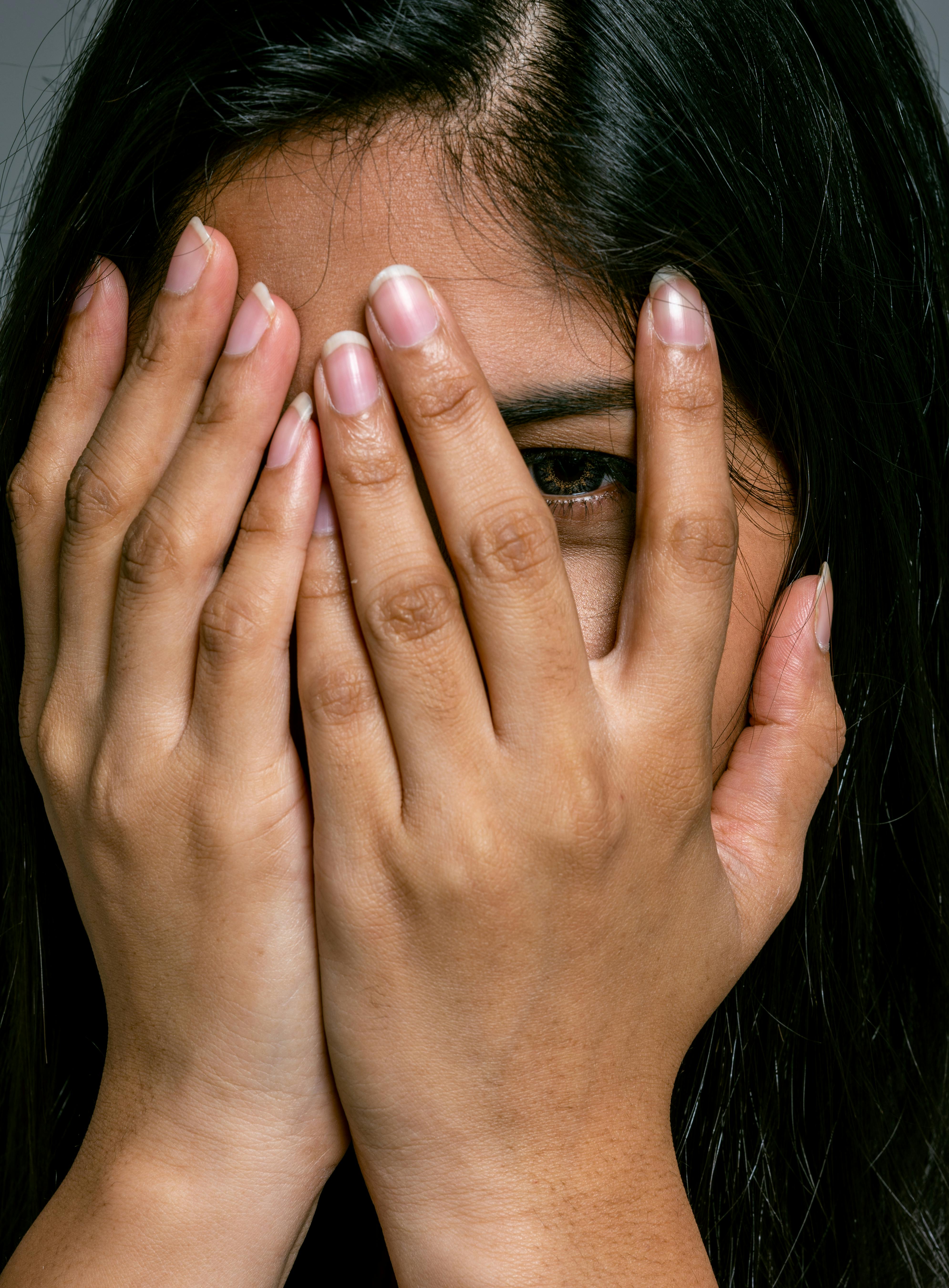 Woman with hands over her face, peeking through fingers